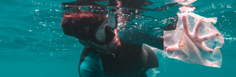 Diver swimming underwater collecting clear plastic